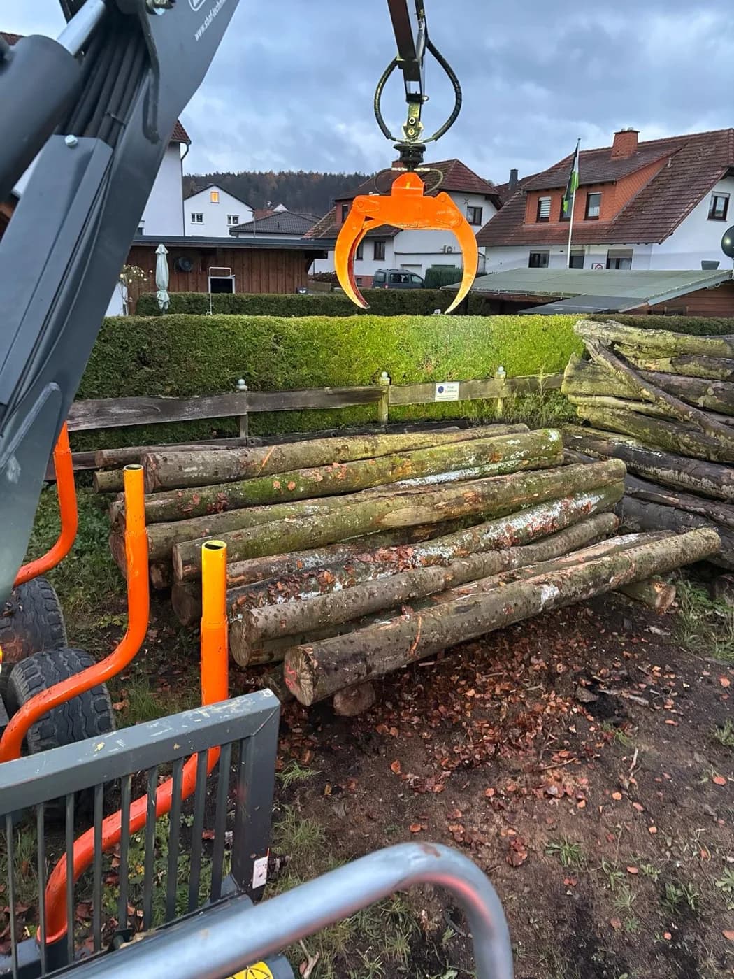 Krangreifer über abgeladenen Stämmen an einem Grundstück