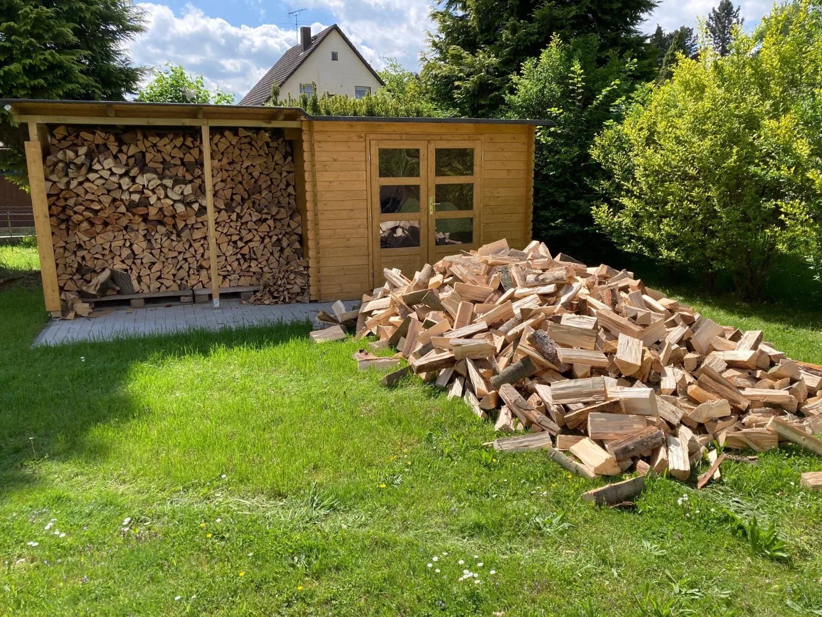 Abgeladenes Brennholz vor einem Holzunterstand im Garten