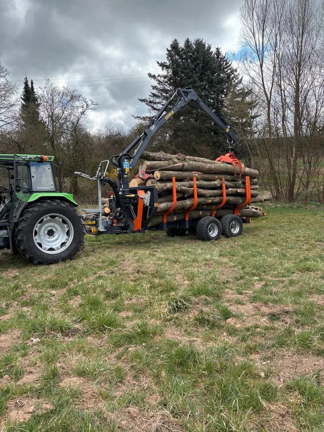 Traktor mit Rückewagen und ausgefahrenem Kran auf einer Wiese