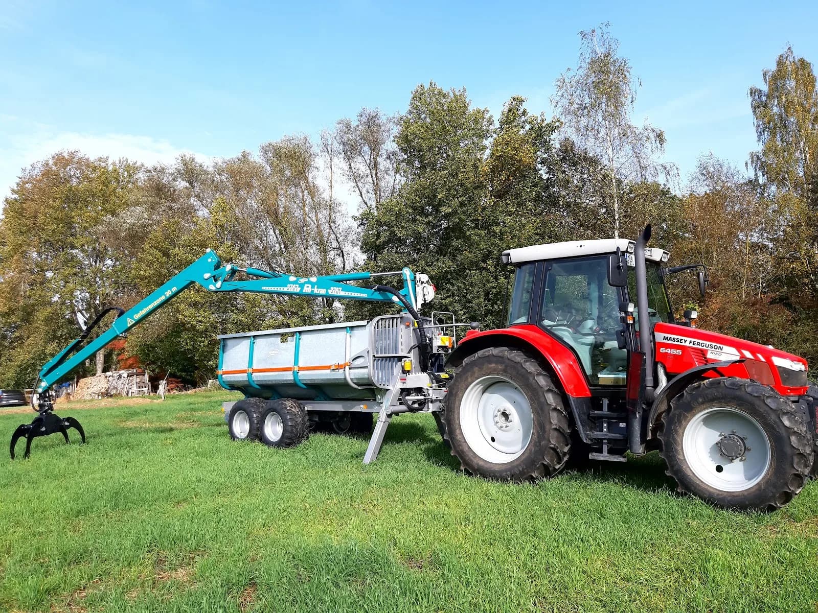 Traktor mit Kran und Rückewagen auf einer Wiese