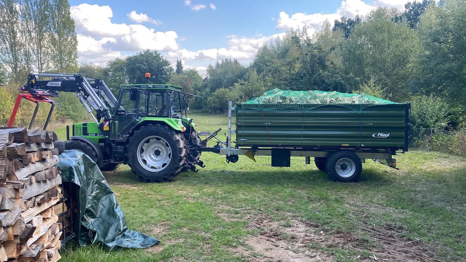 Traktor mit Kipper neben einem Holzstapel