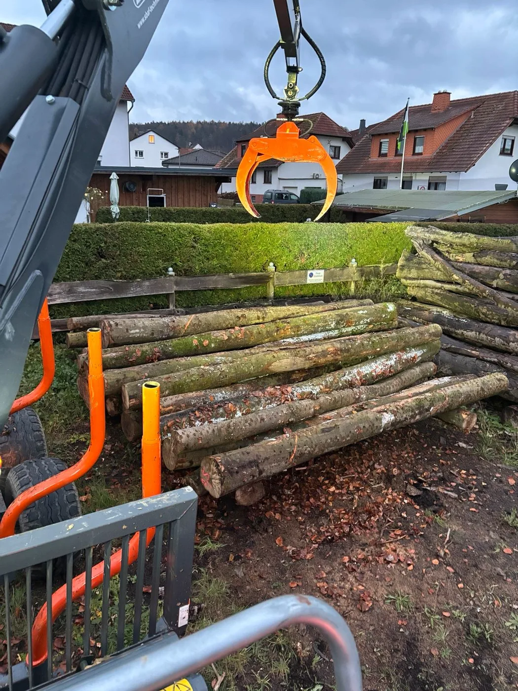 Krangreifer über abgeladenen Stämmen an einem Grundstück
